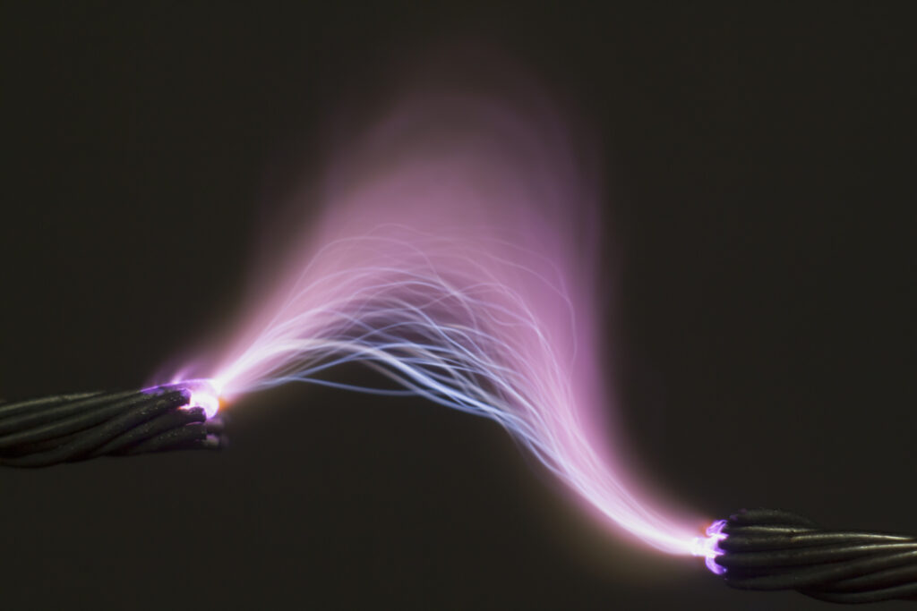 high voltage electrical spark causing an electrical arc flash between two ends of a wire, on black background.